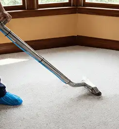 Steam carpet cleaning technician using a hot-water extraction wand on a residential carpet, wearing blue protective shoe covers Pittsburgh, PA.